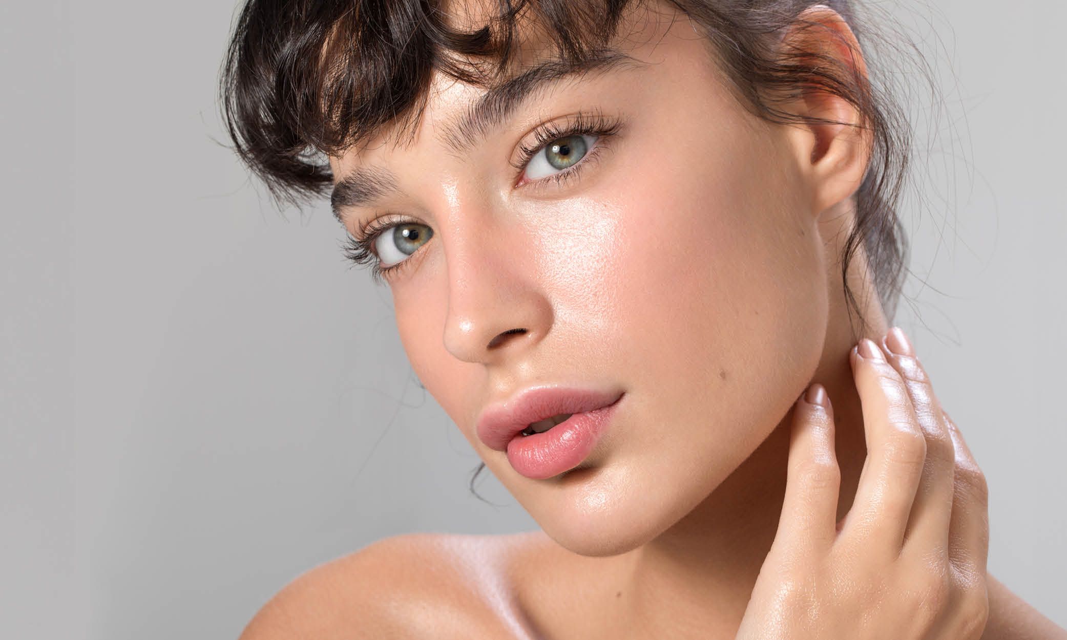 Junge Frau mit gepflegter, glänzender Haut legt die Hand an den Hals – Skinbooster