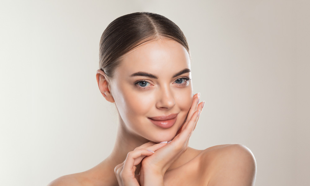 Portrait einer jungen Frau mit strahlender Haut, Hände am Kinn – Skinbooster